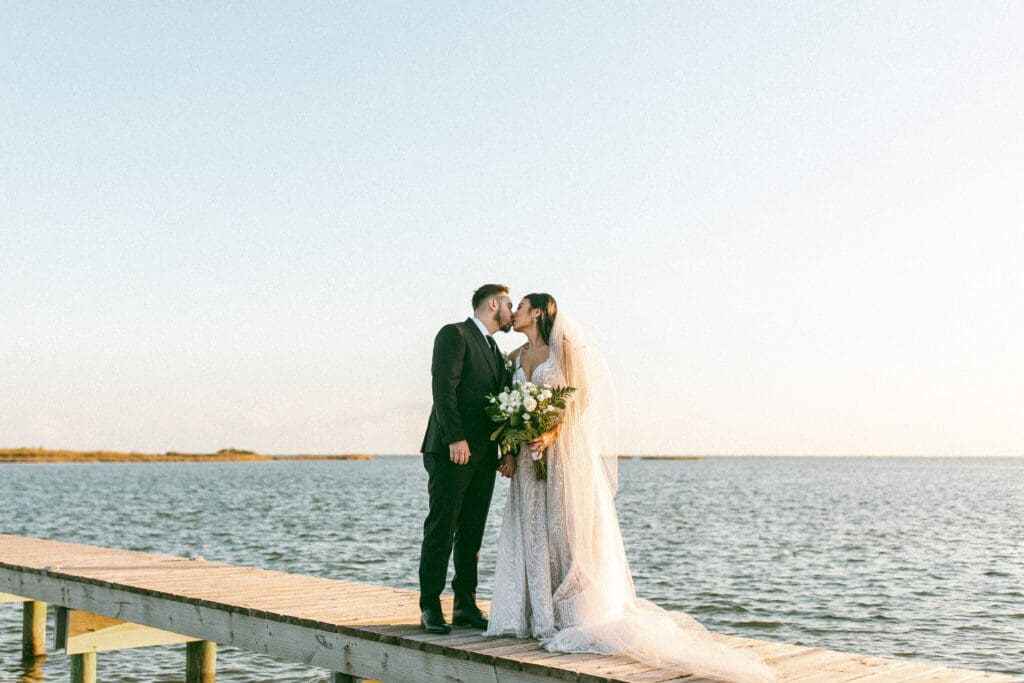 Bride and groom stand on a wooden pier overlooking a calm bay. They are kissing. Photo taken by Lillian Jean Photography a Washington based wedding and elopement photographer who specializes in lifestyle wedding photography. 